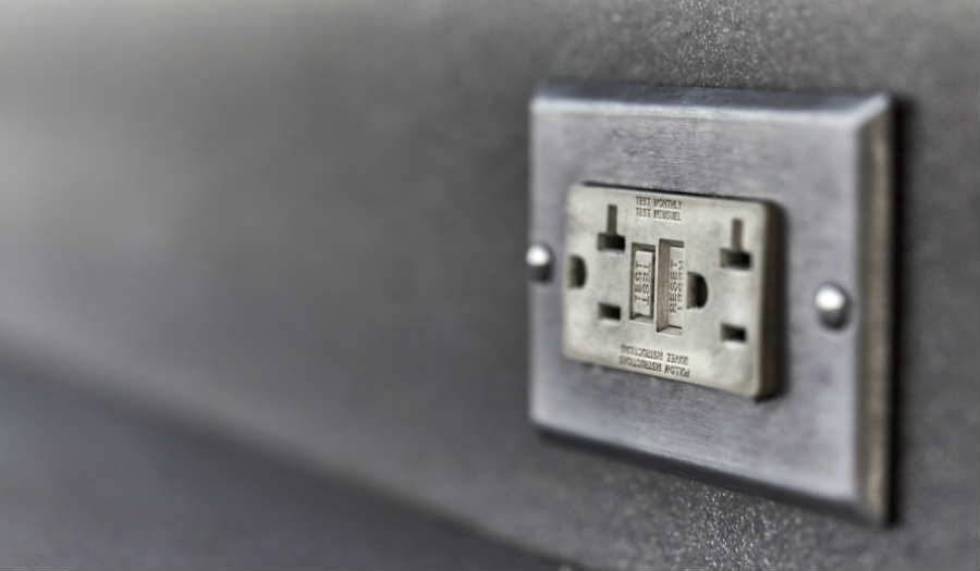 A GFCI electrical outlet is installed on a grey wall. The outlet has two sockets and reset buttons in the center.