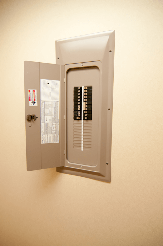 An open electrical panel with the door ajar, revealing various circuit breakers inside.