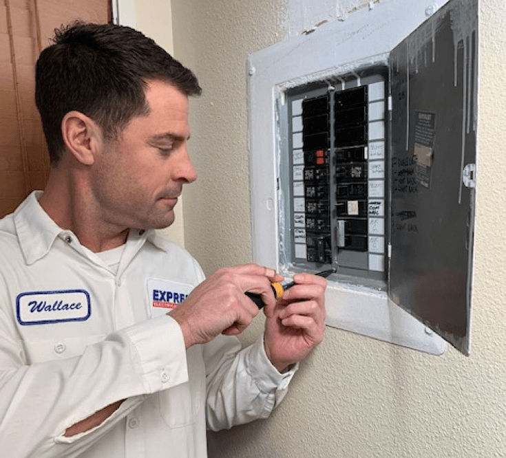 Electrician repairing a circuit breaker in a wall-mounted electrical panel using a screwdriver.