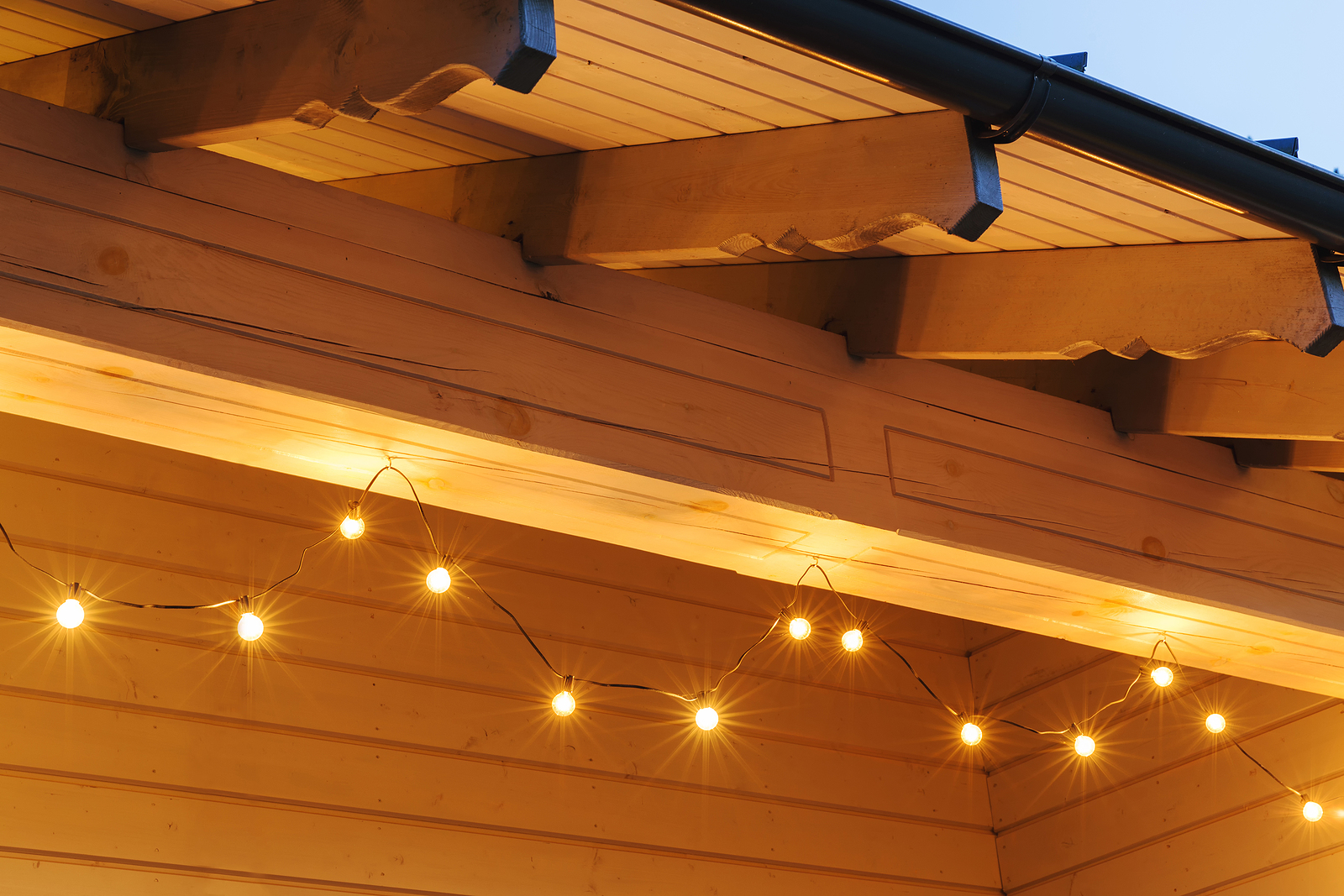 A series of warm yellow string lights are hung under a wooden roof overhang with visible beams.