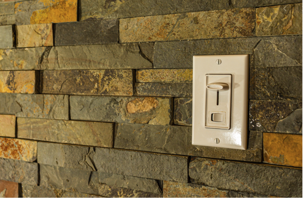 A white light switch plate is mounted on a textured stone wall.