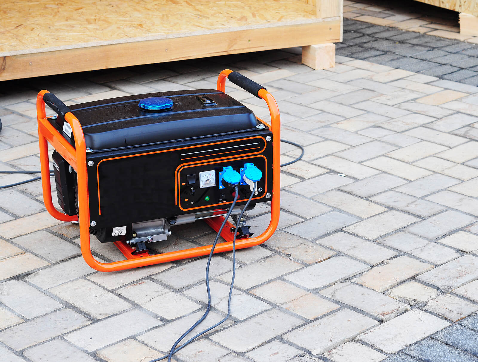 A portable generator with an orange frame sits on a patio, plugged in and in use.